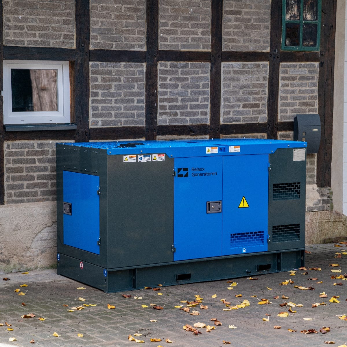 RX-80/100 Stage III Stromgenerator, blau-grünes Gehäuse mit Warnsymbolen, an einer Wand mit Backstein und Holzständern platziert, im Freien.